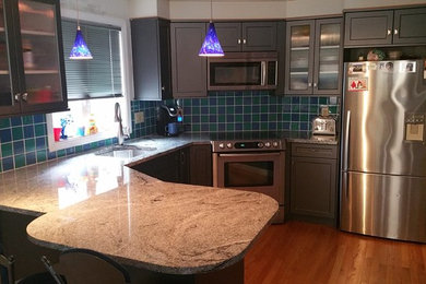 Example of a mid-sized trendy u-shaped light wood floor enclosed kitchen design in Boston with an undermount sink, flat-panel cabinets, gray cabinets, granite countertops, blue backsplash, glass tile backsplash, stainless steel appliances and a peninsula