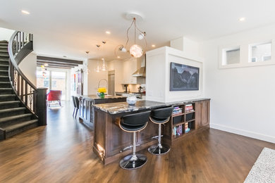 Mid-sized minimalist l-shaped medium tone wood floor and brown floor eat-in kitchen photo in Calgary with a farmhouse sink, shaker cabinets, white cabinets, granite countertops, white backsplash, glass sheet backsplash, stainless steel appliances and an island