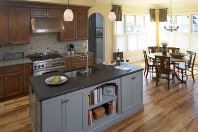 Inspiration for a large craftsman l-shaped medium tone wood floor eat-in kitchen remodel in Charlotte with an undermount sink, flat-panel cabinets, dark wood cabinets, granite countertops, green backsplash, glass tile backsplash, stainless steel appliances and an island