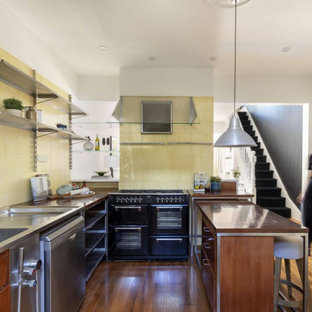 Contemporary l-shaped kitchen in Sydney with an integrated sink, open cabinets, stainless steel cabinets, stainless steel benchtops, yellow splashback, black appliances, medium hardwood floors and with island.
