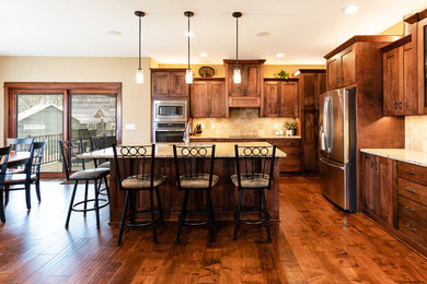 Inspiration for a large craftsman l-shaped medium tone wood floor and brown floor open concept kitchen remodel in Other with an undermount sink, shaker cabinets, dark wood cabinets, granite countertops, beige backsplash, porcelain backsplash, stainless steel appliances, an island and multicolored countertops