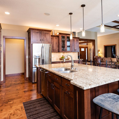 Open concept kitchen - large craftsman l-shaped medium tone wood floor and brown floor open concept kitchen idea in Other with an undermount sink, shaker cabinets, dark wood cabinets, granite countertops, beige backsplash, porcelain backsplash, stainless steel appliances, an island and multicolored countertops
