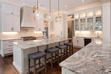 Eat-in kitchen - large transitional l-shaped medium tone wood floor eat-in kitchen idea in Atlanta with a farmhouse sink, shaker cabinets, white cabinets, granite countertops, white backsplash, ceramic backsplash, stainless steel appliances and two islands