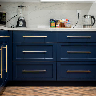Design ideas for a mid-sized shabby-chic style l-shaped kitchen pantry in Los Angeles with a farmhouse sink, shaker cabinets, blue cabinets, quartz benchtops, white splashback, marble splashback, stainless steel appliances, medium hardwood floors, a peninsula, beige floor and white benchtop.