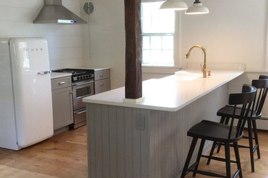 Example of a small transitional galley light wood floor eat-in kitchen design in New York with a farmhouse sink, shaker cabinets, gray cabinets, quartz countertops, stainless steel appliances and a peninsula