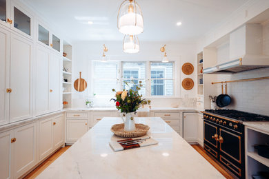Kitchen - transitional u-shaped medium tone wood floor and brown floor kitchen idea in Providence with a farmhouse sink, shaker cabinets, white cabinets, gray backsplash, black appliances, an island and white countertops