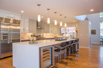 Example of a large trendy l-shaped dark wood floor and brown floor eat-in kitchen design in Denver with an undermount sink, flat-panel cabinets, white cabinets, quartz countertops, white backsplash, stainless steel appliances and an island