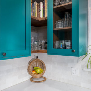 Réalisation d'une cuisine américaine style shabby chic en L de taille moyenne avec un évier de ferme, un placard à porte shaker, des portes de placard turquoises, un plan de travail en quartz modifié, une crédence blanche, une crédence en carreau de céramique, un électroménager en acier inoxydable, sol en stratifié, un îlot central, un sol marron et un plan de travail blanc.