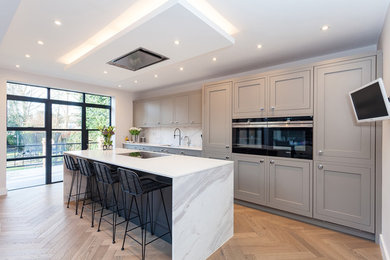 Mid-sized trendy single-wall eat-in kitchen photo in London with an integrated sink, shaker cabinets, gray cabinets, quartzite countertops, white backsplash, marble backsplash, paneled appliances and an island
