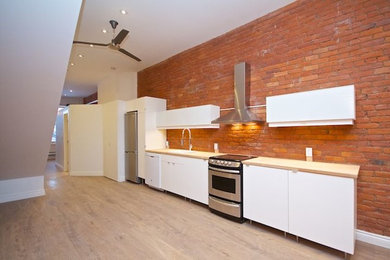 Ejemplo de cocina lineal urbana con armarios con paneles lisos, puertas de armario blancas y encimera de madera