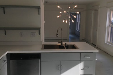 Diseño de cocina minimalista con fregadero encastrado, armarios con paneles lisos, puertas de armario grises, encimera de laminado, electrodomésticos de acero inoxidable y suelo de cemento
