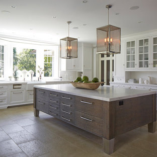 This is an example of a large transitional u-shaped separate kitchen in New York with a farmhouse sink, white cabinets, white splashback, with island, glass-front cabinets, marble benchtops, travertine floors and beige floor.