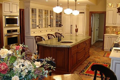 This is an example of a medium sized classic u-shaped kitchen/diner in New York with a submerged sink, raised-panel cabinets, white cabinets, granite worktops, beige splashback, ceramic splashback, stainless steel appliances, brick flooring, an island and brown floors.