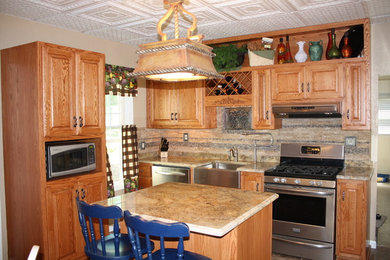 Example of a small classic galley medium tone wood floor eat-in kitchen design in Milwaukee with a farmhouse sink, raised-panel cabinets, black cabinets, beige backsplash, stone tile backsplash, white appliances and an island