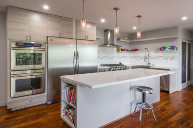 Large trendy l-shaped medium tone wood floor open concept kitchen photo in Orange County with a farmhouse sink, flat-panel cabinets, gray cabinets, quartzite countertops, white backsplash, subway tile backsplash, stainless steel appliances and an island