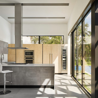 Foto di una cucina moderna con lavello sottopiano, ante lisce, ante in legno chiaro, paraspruzzi bianco, elettrodomestici da incasso, penisola e pavimento grigio