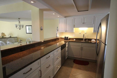 Example of a small galley porcelain tile eat-in kitchen design in Miami with a single-bowl sink, raised-panel cabinets, white cabinets, granite countertops, stainless steel appliances and an island