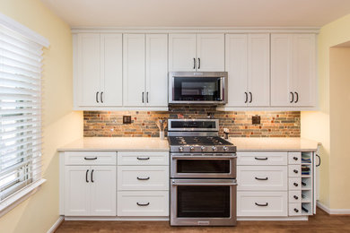 ワシントンD.C.にある高級な中くらいなトランジショナルスタイルのおしゃれなキッチン (アンダーカウンターシンク、シェーカースタイル扉のキャビネット、白いキャビネット、クオーツストーンカウンター、グレーのキッチンパネル、石タイルのキッチンパネル、シルバーの調理設備、クッションフロア、茶色い床、ベージュのキッチンカウンター) の写真