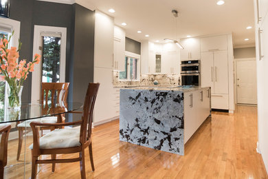 Large minimalist l-shaped light wood floor and yellow floor eat-in kitchen photo in Other with an undermount sink, flat-panel cabinets, white cabinets, granite countertops, multicolored backsplash, stone slab backsplash, paneled appliances, an island and multicolored countertops