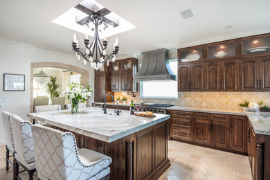 Large transitional limestone floor and beige floor eat-in kitchen photo in Los Angeles with an undermount sink, dark wood cabinets, beige backsplash, an island and white countertops