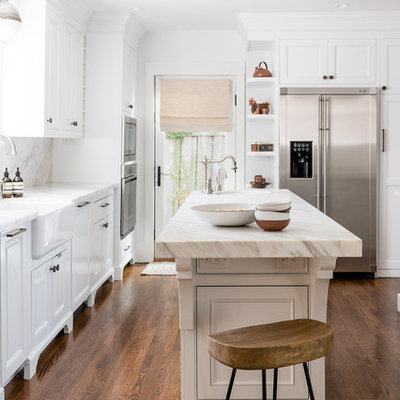 Transitional u-shaped medium tone wood floor and brown floor kitchen photo in Sacramento with a farmhouse sink, white cabinets, stainless steel appliances, an island and white countertops