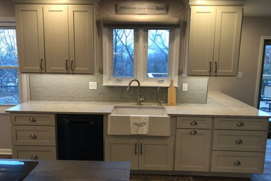 Large transitional l-shaped porcelain tile and brown floor eat-in kitchen photo in Philadelphia with a farmhouse sink, flat-panel cabinets, gray cabinets, quartz countertops, gray backsplash, glass tile backsplash, black appliances, an island and gray countertops