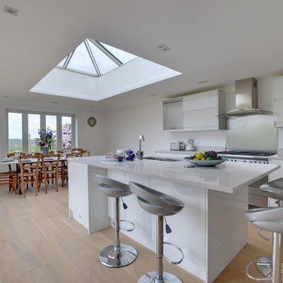 Large minimalist single-wall light wood floor and beige floor eat-in kitchen photo in Kent with an undermount sink, flat-panel cabinets, white cabinets, metallic backsplash, metal backsplash, stainless steel appliances, an island and white countertops