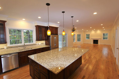 Example of a mid-sized transitional l-shaped medium tone wood floor and beige floor open concept kitchen design in DC Metro with an undermount sink, raised-panel cabinets, dark wood cabinets, granite countertops, beige backsplash, stone slab backsplash, stainless steel appliances and an island