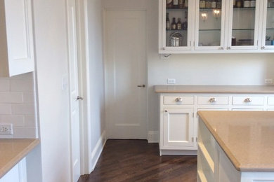 Example of a large classic u-shaped dark wood floor enclosed kitchen design in New York with an undermount sink, shaker cabinets, white cabinets, solid surface countertops and an island