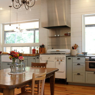 Modelo de cocina comedor en L, de estilo de casa de campo, de tamaño medio, sin isla, con electrodomésticos blancos, puertas de armario azules, armarios estilo shaker, encimera de esteatita, salpicadero blanco, fregadero sobremueble y suelo de madera en tonos medios
