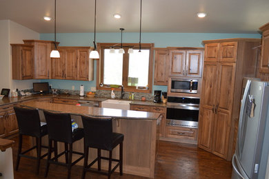 Photo of a rural u-shaped kitchen in Other with a belfast sink, raised-panel cabinets, light wood cabinets, quartz worktops, stainless steel appliances, vinyl flooring and an island.