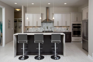 Example of a trendy porcelain tile eat-in kitchen design in Columbus with shaker cabinets, gray cabinets, granite countertops, mosaic tile backsplash, stainless steel appliances and an island
