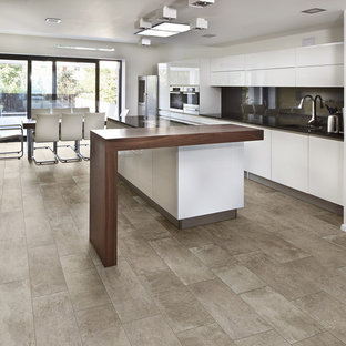 Inspiration for a large contemporary galley eat-in kitchen in Boise with an undermount sink, flat-panel cabinets, white cabinets, solid surface benchtops, black splashback, glass sheet splashback, stainless steel appliances, ceramic floors and with island.