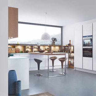 Idée de décoration pour une cuisine ouverte parallèle minimaliste de taille moyenne avec un évier encastré, un placard à porte plane, des portes de placard blanches, un plan de travail en verre, un électroménager en acier inoxydable, béton au sol et un îlot central.