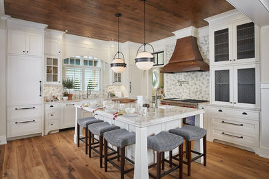 Design ideas for a large traditional l-shaped open plan kitchen in Grand Rapids with a belfast sink, shaker cabinets, white cabinets, engineered stone countertops, grey splashback, mosaic tiled splashback, integrated appliances, medium hardwood flooring, an island, brown floors and beige worktops.