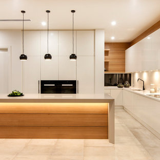 Photo of a large contemporary l-shaped kitchen in Adelaide with flat-panel cabinets, white cabinets, white splashback, glass sheet splashback, black appliances, with island and beige floor.