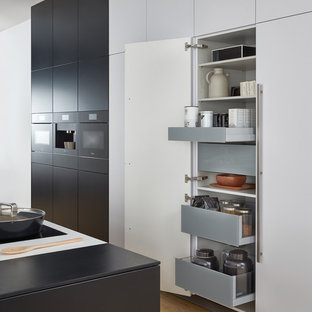 Immagine di un'ampia cucina minimalista con lavello sottopiano, ante lisce, ante nere, top in superficie solida, elettrodomestici neri, parquet chiaro e isola