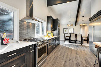 Inspiration for a large contemporary l-shaped light wood floor and brown floor eat-in kitchen remodel in Boise with a farmhouse sink, shaker cabinets, dark wood cabinets, quartz countertops, gray backsplash, glass tile backsplash, stainless steel appliances and an island