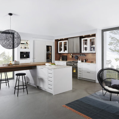 Inspiration for a large modern l-shaped concrete floor eat-in kitchen remodel in New York with a farmhouse sink, shaker cabinets, white cabinets, laminate countertops, brown backsplash, stainless steel appliances and a peninsula