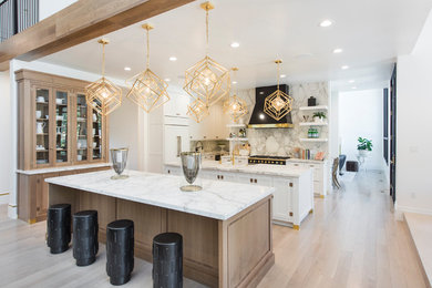 Example of a large trendy l-shaped medium tone wood floor and brown floor eat-in kitchen design in Salt Lake City with a farmhouse sink, shaker cabinets, white cabinets, marble countertops, white backsplash, marble backsplash, paneled appliances and two islands