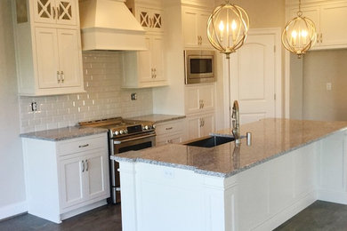Large elegant kitchen photo in Louisville with white cabinets, granite countertops, white backsplash, stainless steel appliances and an island