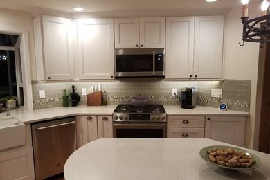 Mid-sized elegant u-shaped eat-in kitchen photo in Seattle with a farmhouse sink, recessed-panel cabinets, white cabinets, quartz countertops, gray backsplash, glass tile backsplash, stainless steel appliances, an island and white countertops