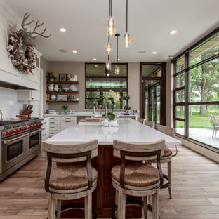 Idee per una cucina rustica di medie dimensioni con isola, ante in stile shaker, ante bianche, paraspruzzi bianco, paraspruzzi in lastra di pietra, elettrodomestici in acciaio inossidabile, pavimento in legno massello medio e top bianco