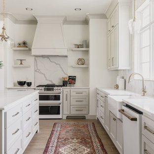 Transitional kitchen ideas - Example of a transitional l-shaped brown floor kitchen design in Oklahoma City with a farmhouse sink, recessed-panel cabinets, white cabinets, white backsplash, white appliances, an island and white countertops