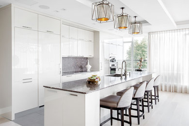 Example of a transitional galley light wood floor kitchen design in Montreal with an undermount sink, flat-panel cabinets, white cabinets, gray backsplash, stainless steel appliances and an island