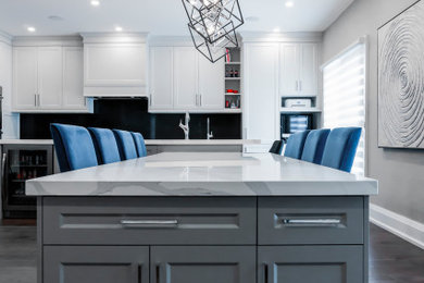 Example of a large transitional l-shaped dark wood floor and brown floor eat-in kitchen design in Toronto with an undermount sink, shaker cabinets, white cabinets, quartzite countertops, black backsplash, stone slab backsplash, stainless steel appliances, an island and white countertops