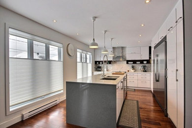 Example of a large trendy l-shaped dark wood floor eat-in kitchen design in Montreal with an undermount sink, flat-panel cabinets, white cabinets, quartz countertops, white backsplash, stone tile backsplash, stainless steel appliances and an island