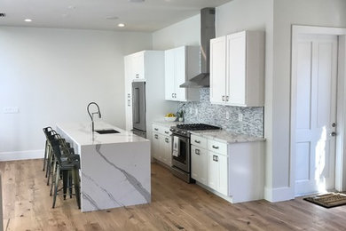 Foto på ett mellanstort funkis kök, med en undermonterad diskho, skåp i shakerstil, vita skåp, bänkskiva i kvarts, flerfärgad stänkskydd, stänkskydd i marmor, rostfria vitvaror, ljust trägolv, en köksö och flerfärgat golv