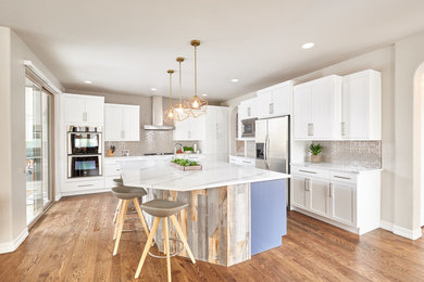 Example of a large trendy l-shaped medium tone wood floor and brown floor enclosed kitchen design in Denver with an undermount sink, shaker cabinets, quartz countertops, gray backsplash, ceramic backsplash, stainless steel appliances, an island, white countertops and white cabinets