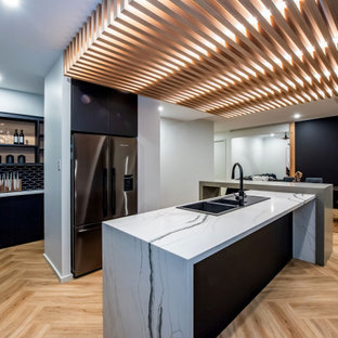 Contemporary l-shaped eat-in kitchen in Other with a double-bowl sink, flat-panel cabinets, black cabinets, black splashback, stainless steel appliances, light hardwood floors, with island, beige floor and multi-coloured benchtop.